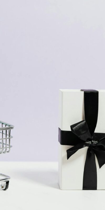 Minimalist shopping concept with cart and gift box tied with black ribbon.