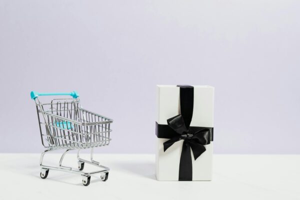 Minimalist shopping concept with cart and gift box tied with black ribbon.