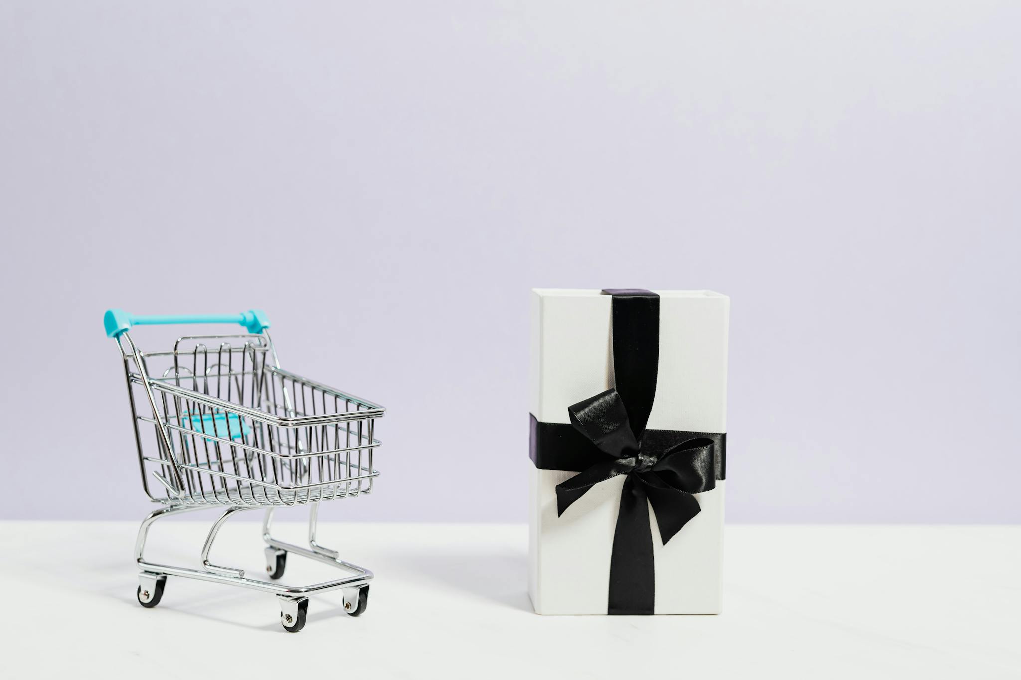 Minimalist shopping concept with cart and gift box tied with black ribbon.